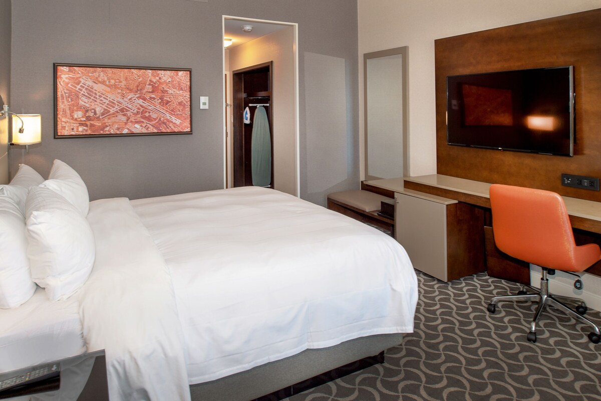 A hotel room with a large bed, a desk with a chair, a television, and a map on the wall.