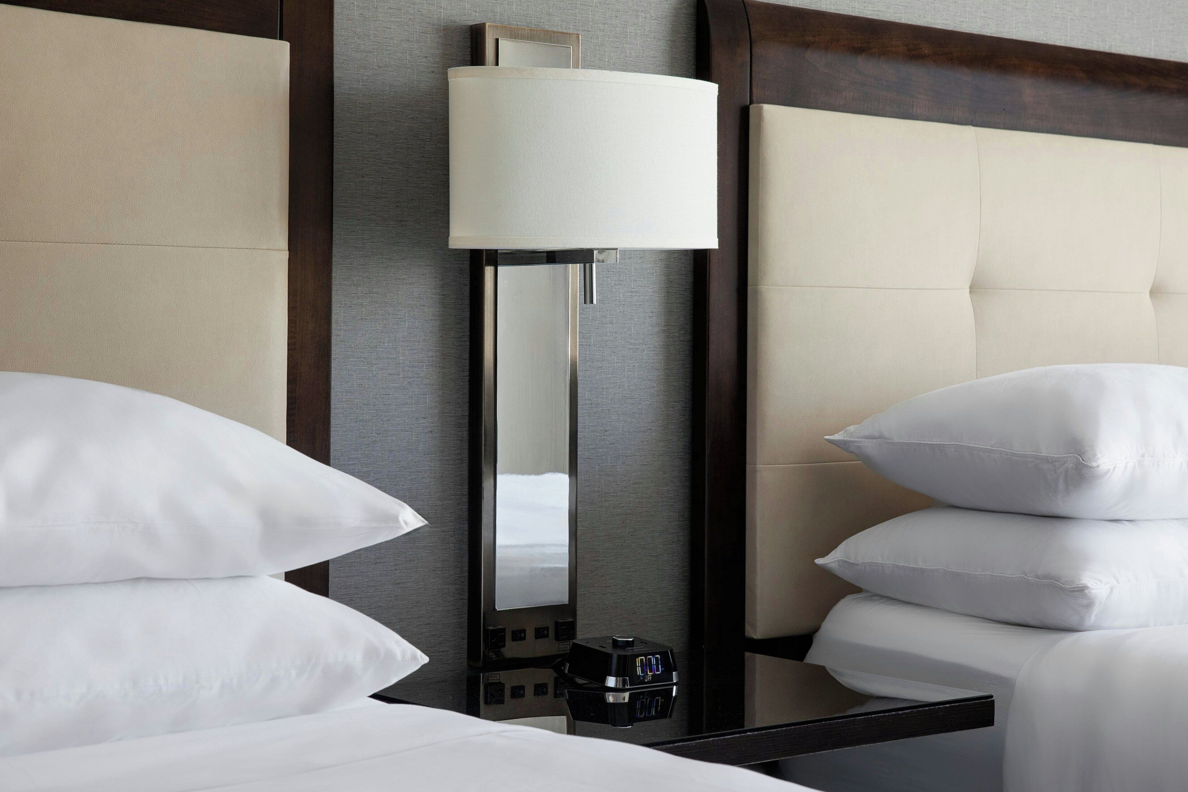 A hotel room with a bed, a bedside table with a lamp, and a control panel.