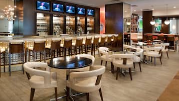 A bar area with multiple seating options, including bar stools and round tables, and a television screen displaying a program.