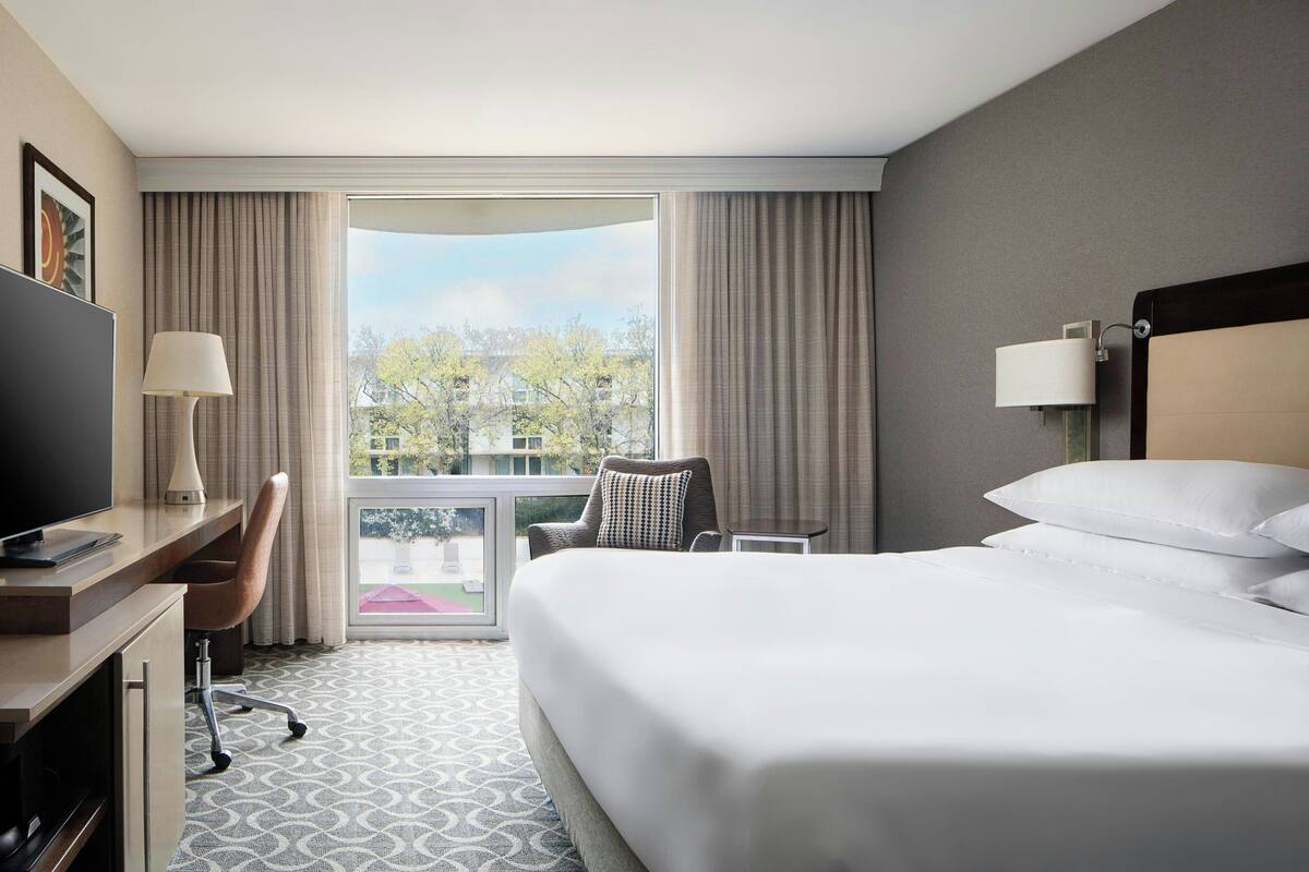 Habitación de hotel con una cama grande, un escritorio con computadora, una silla y vistas al exterior.