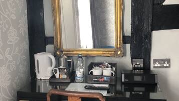 Un escritorio con un espejo grande, una cafetera, una botella de agua e una impresora.