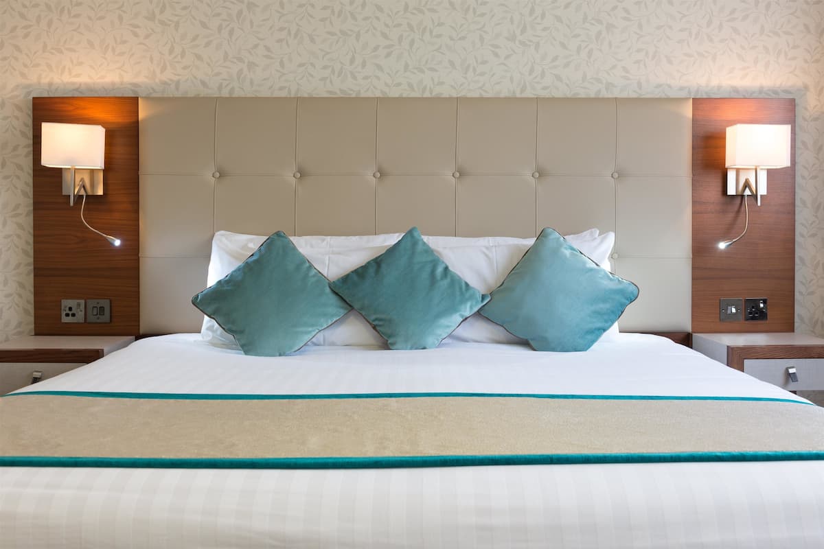 A hotel room with a large bed, a tufted headboard, and two wall-mounted lamps.