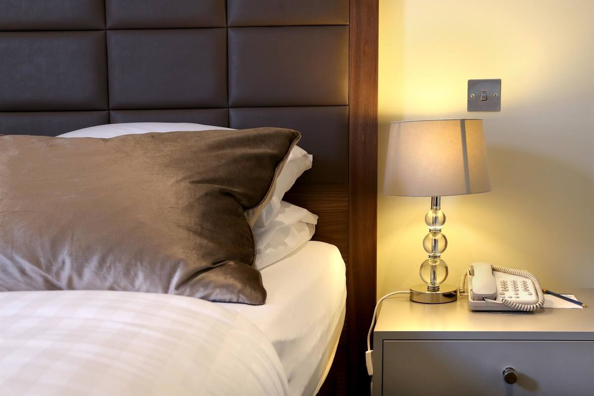 A neatly made bed with a pillow, a bedside lamp, and a telephone on a nightstand.