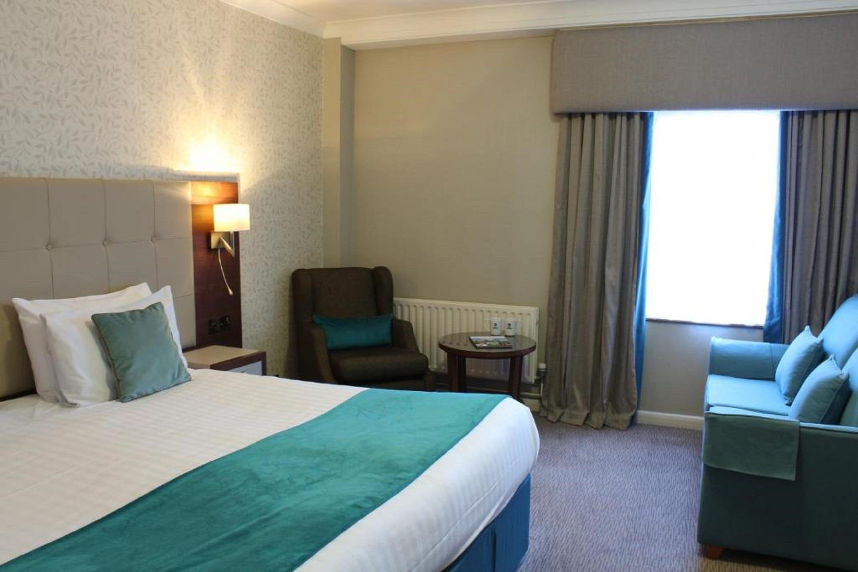 Una habitación de hotel con una cama grande, una silla, una mesita y un sofá.