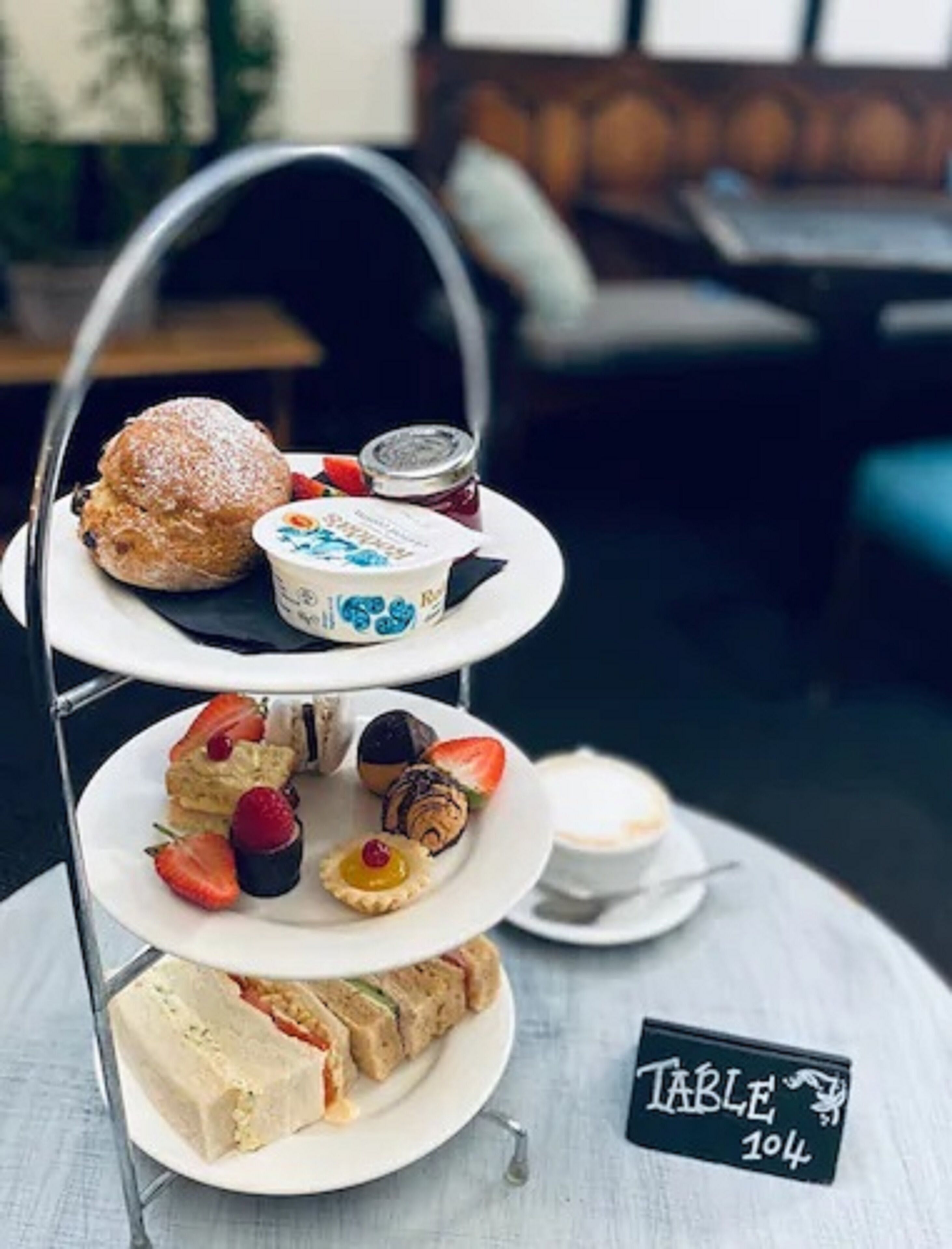 A three-tiered dessert stand with various pastries and a cup of coffee on a table labeled "Table 104".