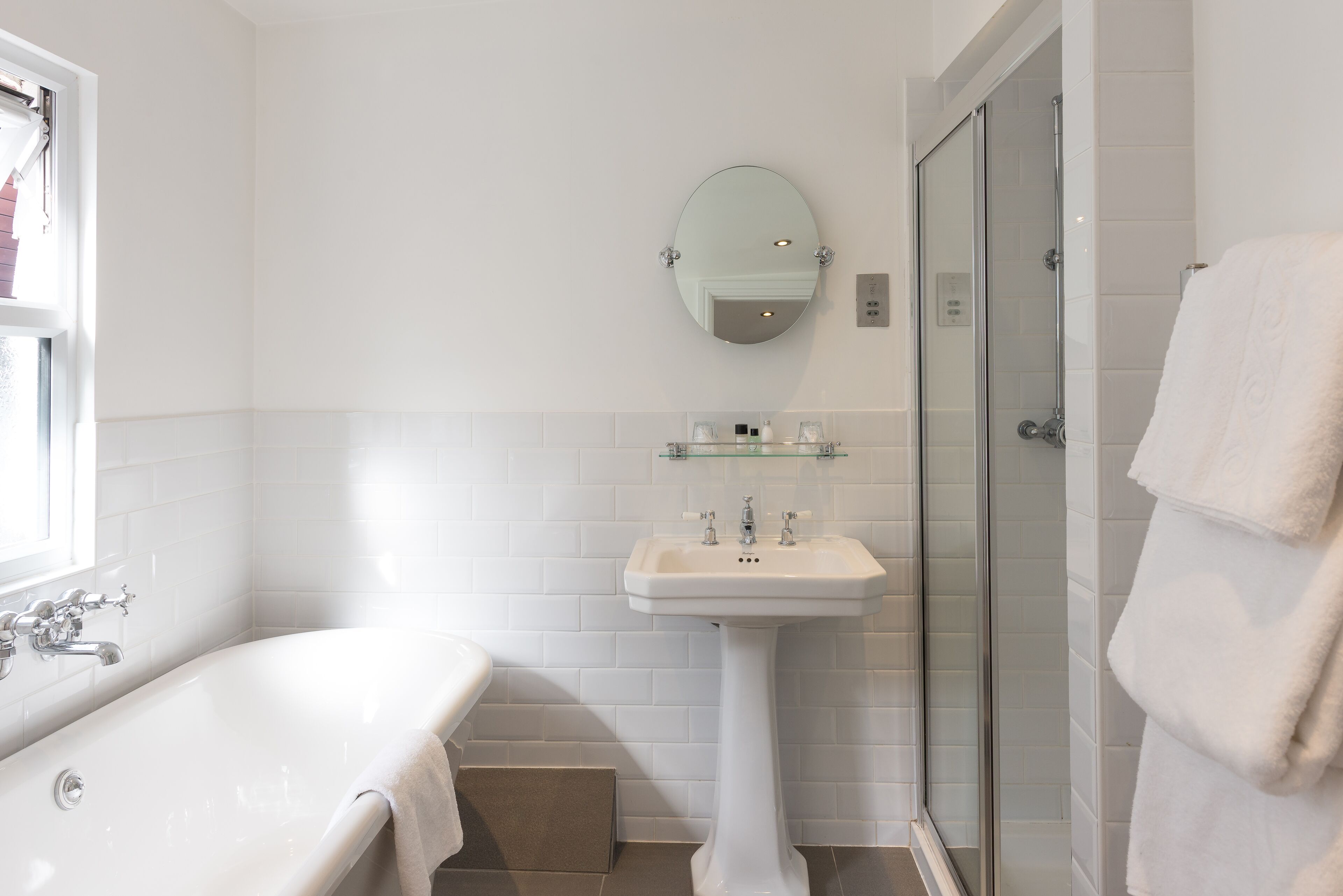 A modern bathroom with a freestanding bathtub, a pedestal sink, a glass shower enclosure, and a wall-mounted mirror.