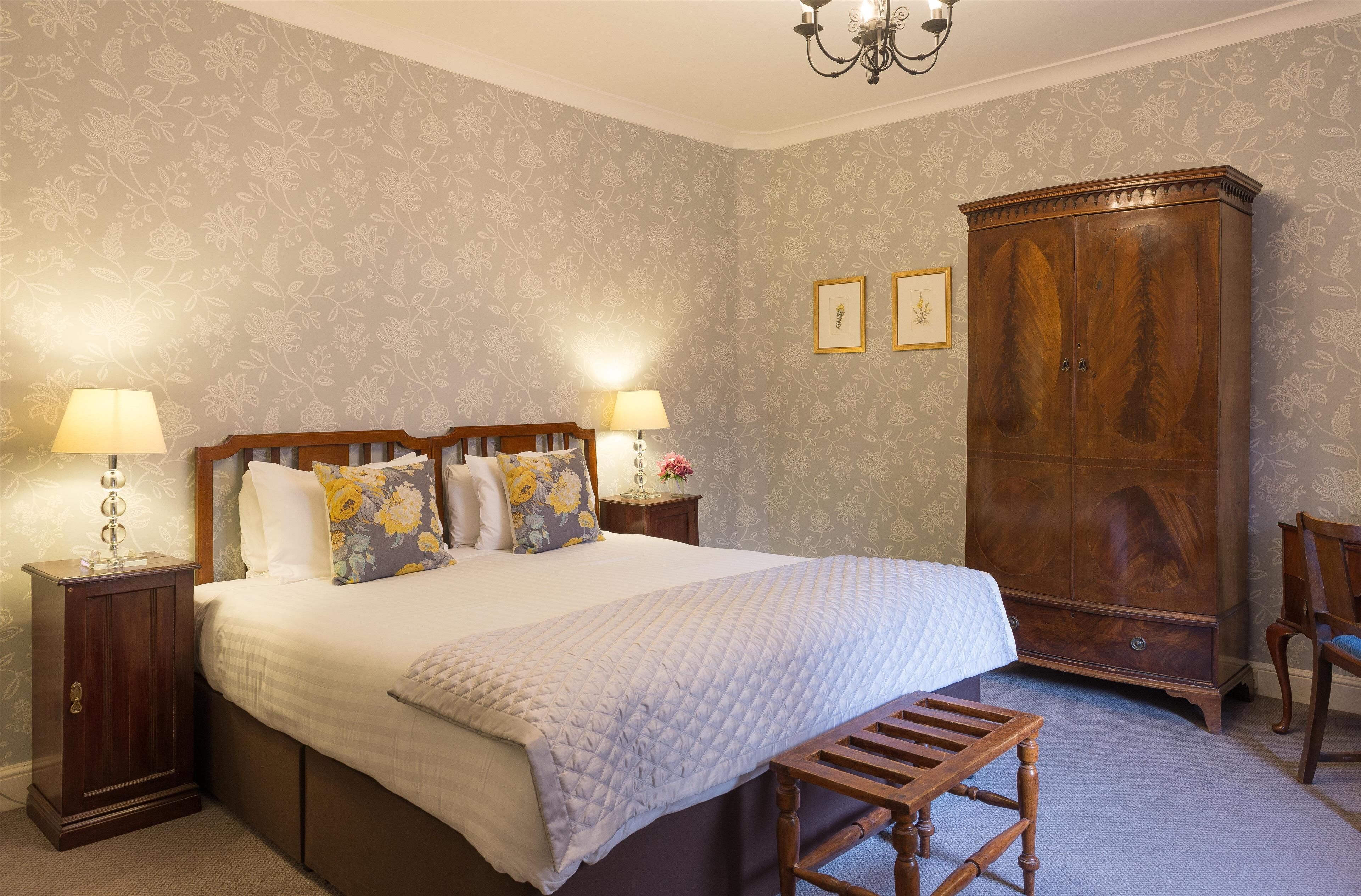 Un dormitorio con una cama grande, dos lámparas de noche, un armario de madera y un pequeño banco.