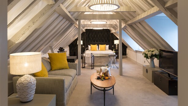 A modern loft bedroom with a sloped ceiling, a bed with yellow pillows, a TV, and a dining area with a table and lamp. - Best Western Red Lion Hotel (Salisbury)