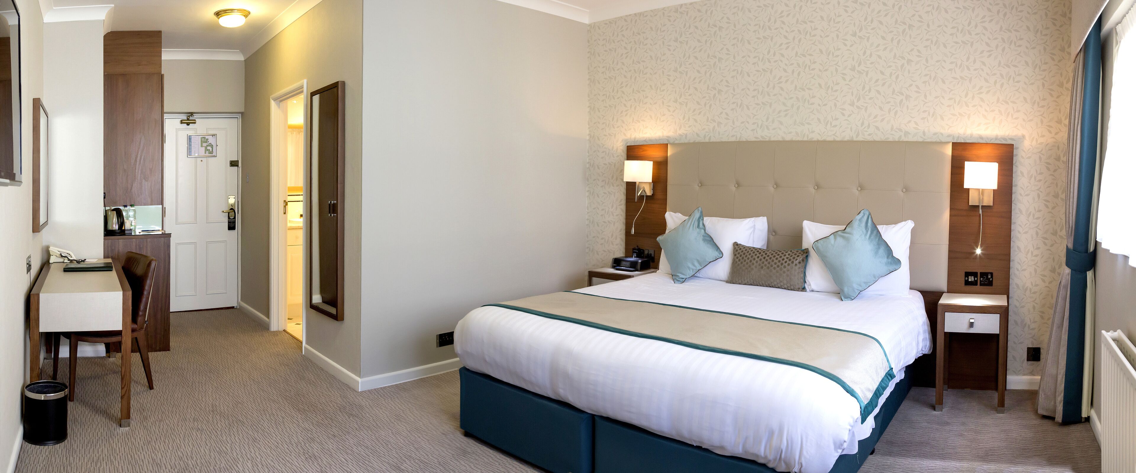 A hotel room with a bed, bedside tables, a desk, and a chair.