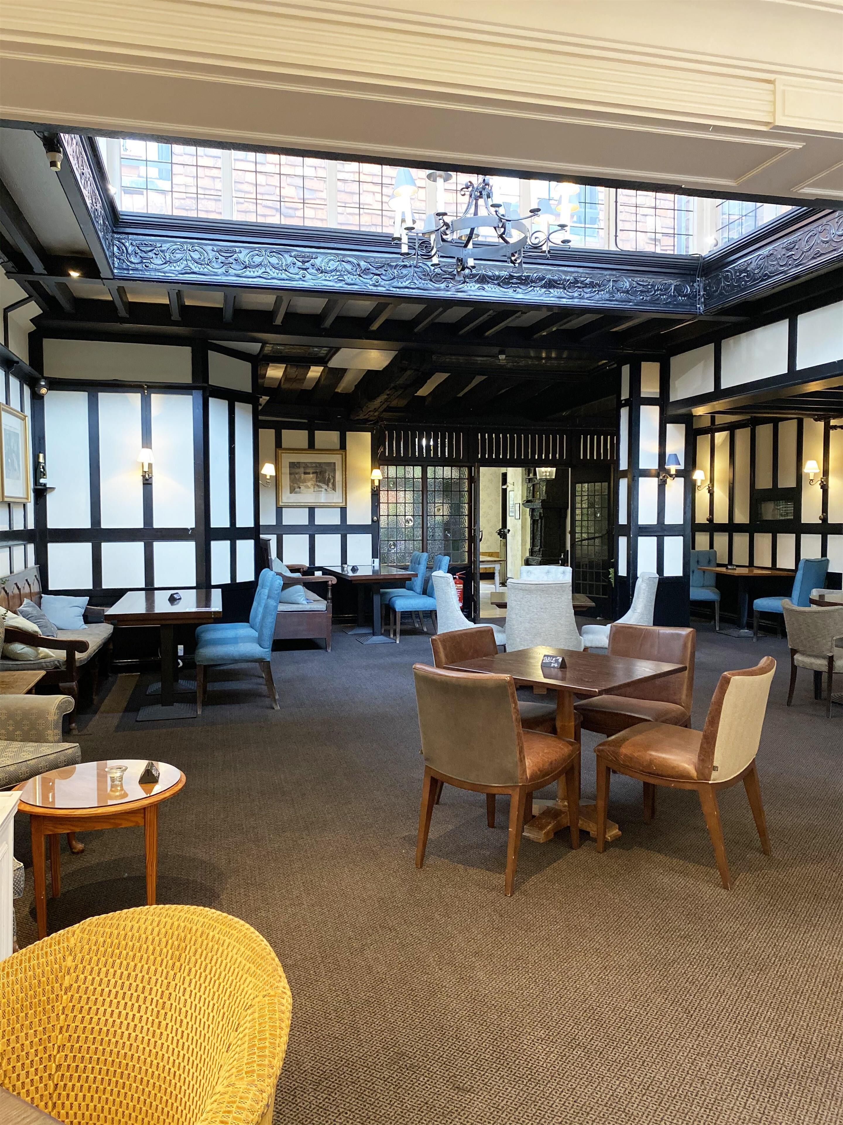 A spacious room with a high ceiling, exposed beams, and a skylight. There are multiple seating areas with tables and chairs, and a fireplace.
