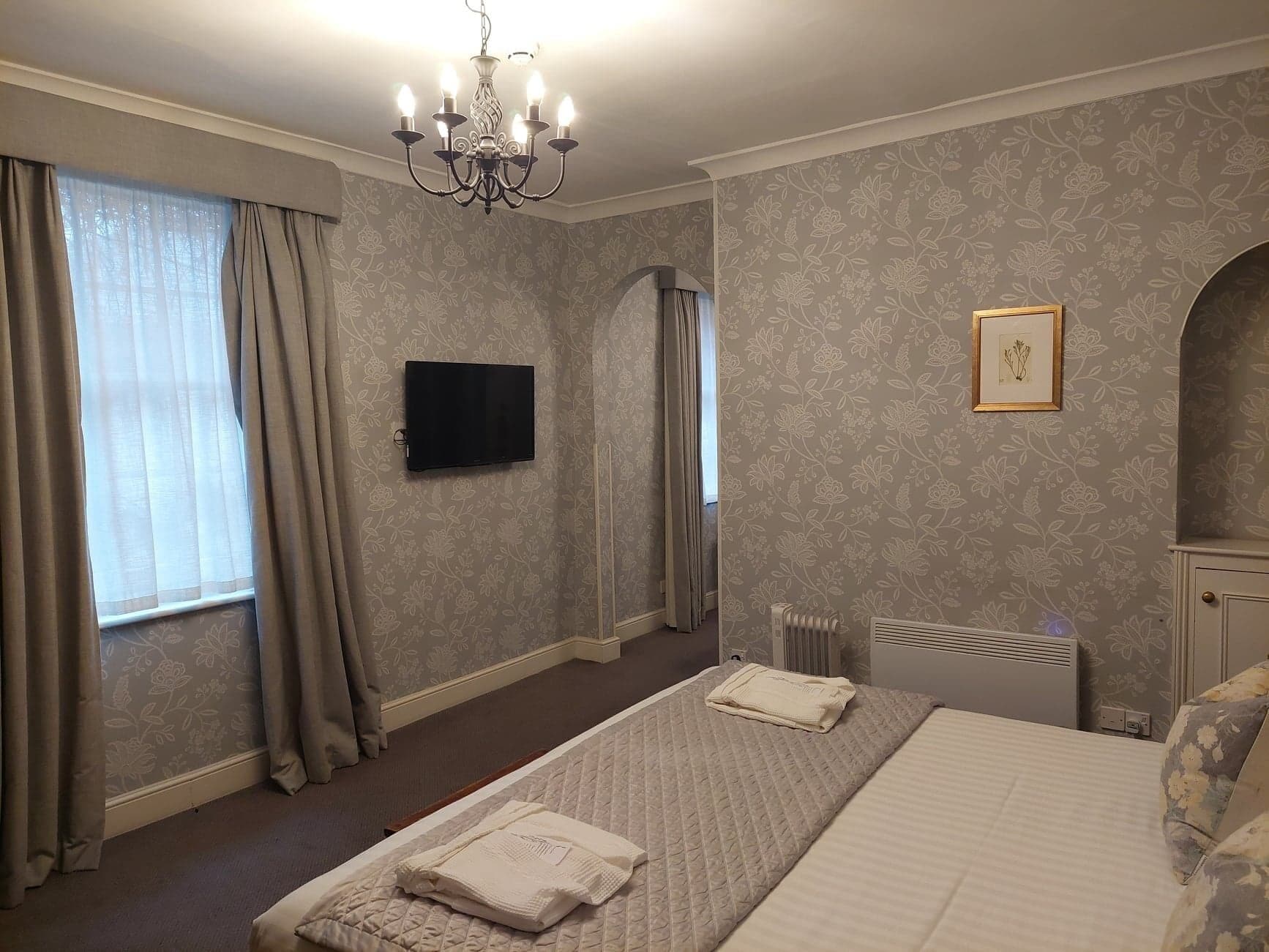 Ein Hotelzimmer mit einem Bett, einem Flachbildfernseher, einer Kristallleuchtre und einer Heizung.