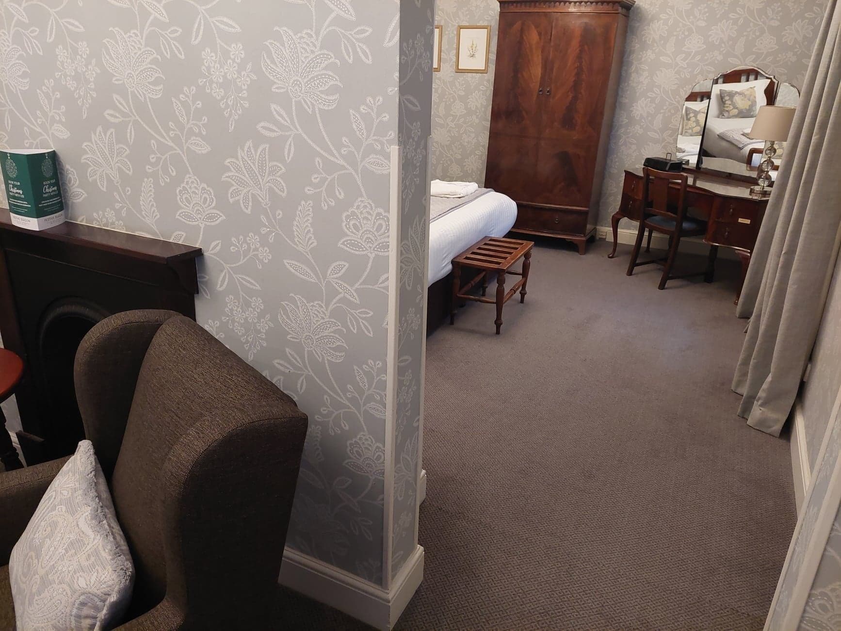 Een hotelkamer met een bed, een houten garderobe, een bureau met stoel, een klein krukje en een bank.