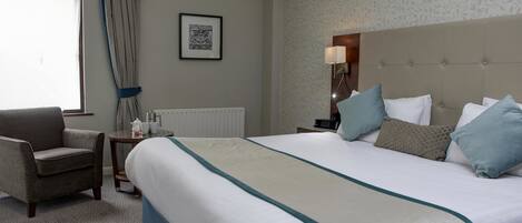 A hotel room with a large bed, a chair, a bedside table with a lamp, and a framed picture on the wall.