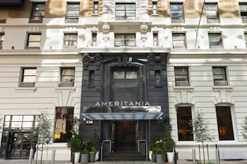 A hotel room with a large abstract painting, a bed with black and white bedding, a nightstand with a lamp, and a mirror on the wall. at Ameritania Hotel at Times Square