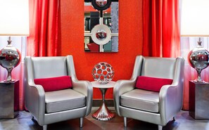 Two grey armchairs with red cushions, a small table with a metallic sphere, and a red textured wall with a mirror. - Ameritania Hotel at Times Square (New York)