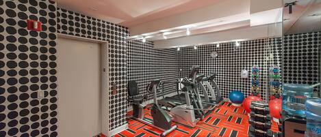 Uma academia com equipamentos de exercício, parede estampada e piso vermelho.