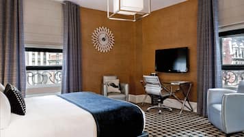 A hotel room with a large bed, a desk, two chairs, a TV, and a decorative wall piece.