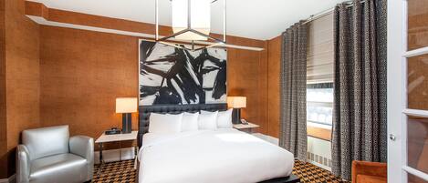 A hotel room with a large bed, a chair, a desk with a lamp, and a large abstract painting on the wall.