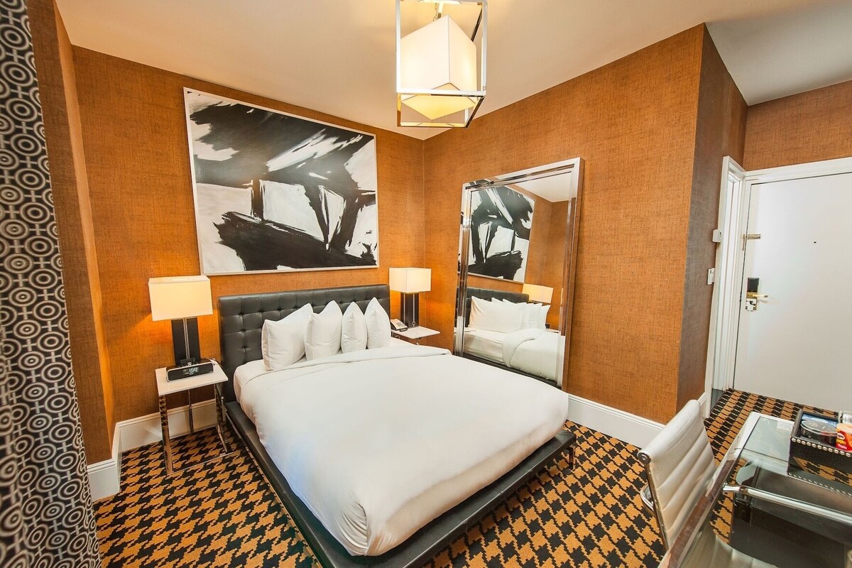 A hotel room with a large bed, two bedside tables, a mirror, and a patterned floor.