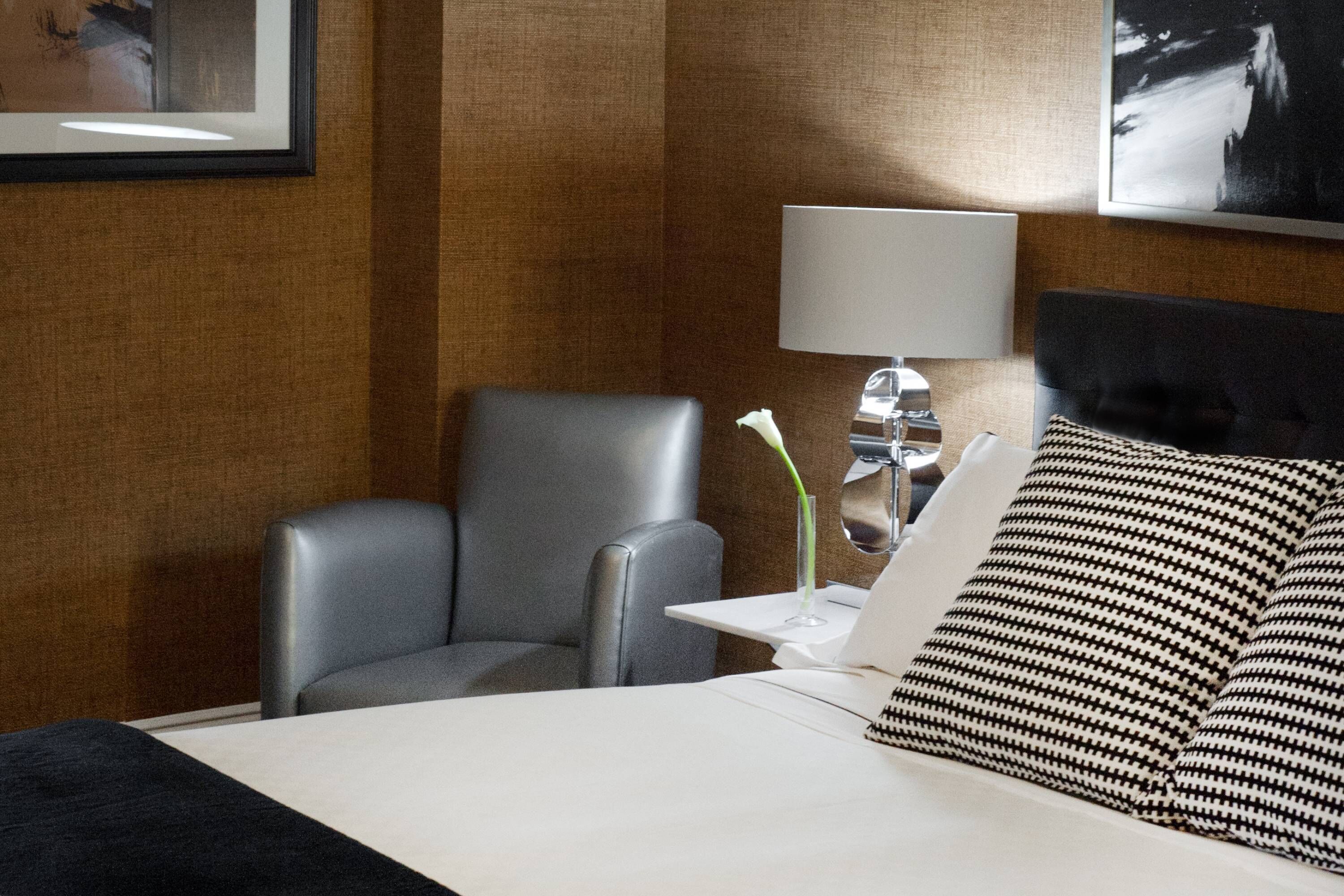 Une chambre d’hôtel avec un lit, un bureau avec un ordinateur portable, une chaise, une lampe et un tableau encadré au mur.