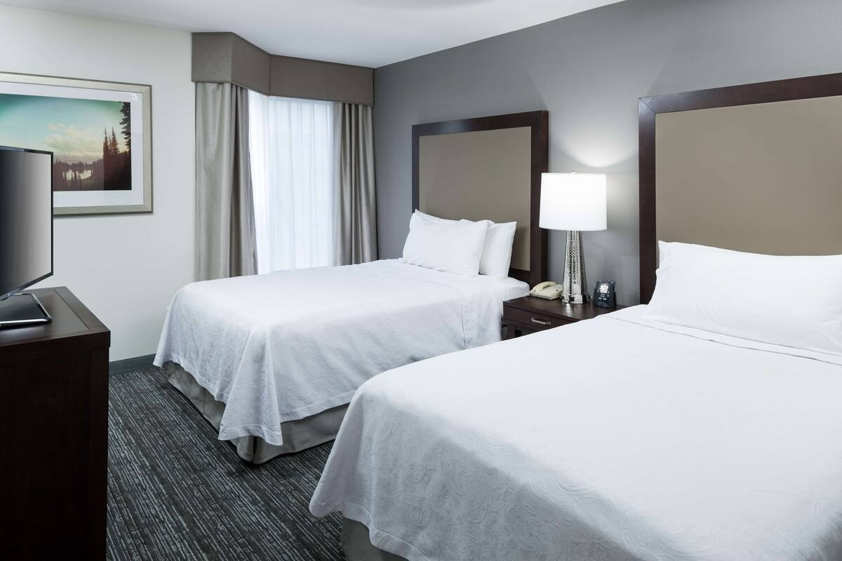 A hotel room with two beds, a desk, a TV, and a lamp.