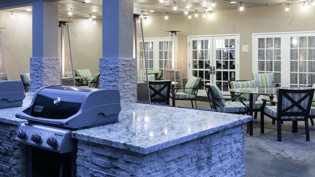 An outdoor patio with a stone barbecue grill, cushioned chairs, and string lights. - Homewood Suites by Hilton Seattle-Tacoma Airport/Tukwila (Tukwila)