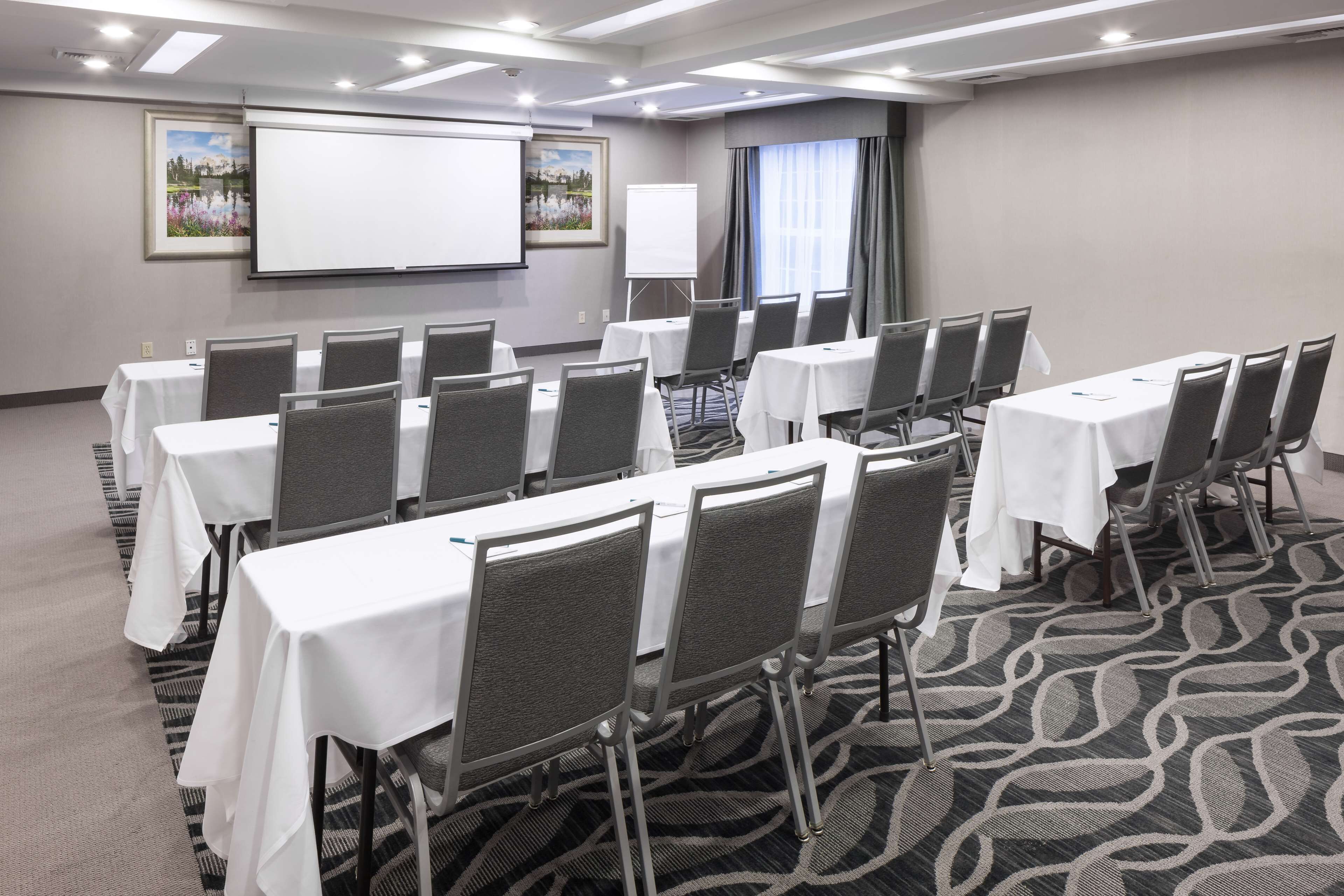 Una sala de conferencias con varias mesas y sillas, una pantalla de proyector y una pizarra.