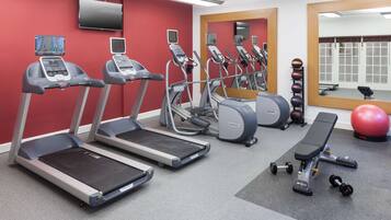 A gym with treadmills, a bench, dumbbells, and a red wall.