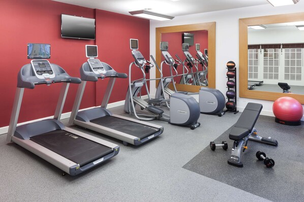Un gimnasio con cintas de correr, una banca, mancuernas y una pared roja.