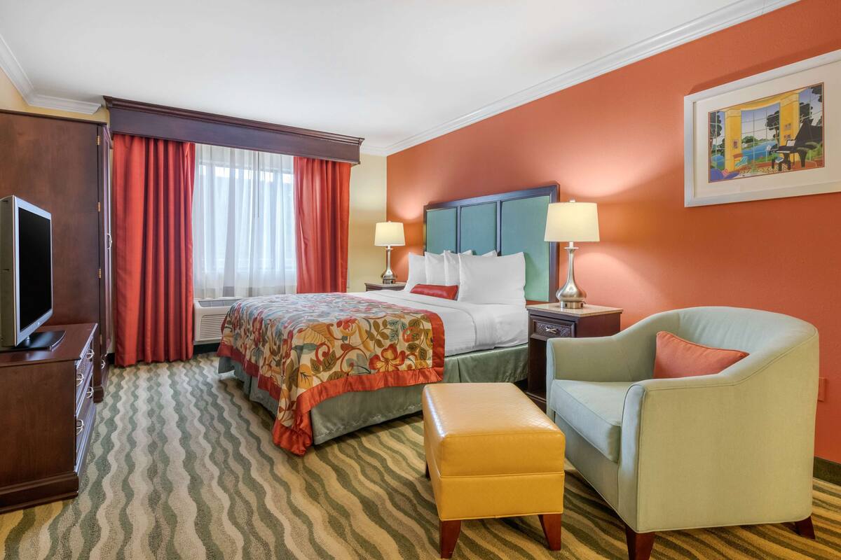 A hotel room with a bed, two bedside tables, a television, a sofa, and a window with curtains.