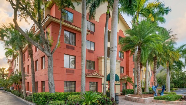 A multi-story hotel with a red facade, palm trees, and a landscaped garden. - Best Western Plus Palm Beach Gardens Hotel & Ste & Conf Ctr (North Palm Beach)