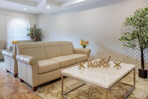 A beige sofa and a small table with a 'travel' sign in a room with patterned walls and a potted plant. - Best Western Plus Palm Beach Gardens Hotel & Suites and Conference Ct (North Palm Beach)