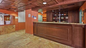 A reception area with a wooden counter, stone-tiled floor, and a ceiling with recessed lighting. - Palm Beach Gardens & Suites Conference Ct (North Palm Beach)