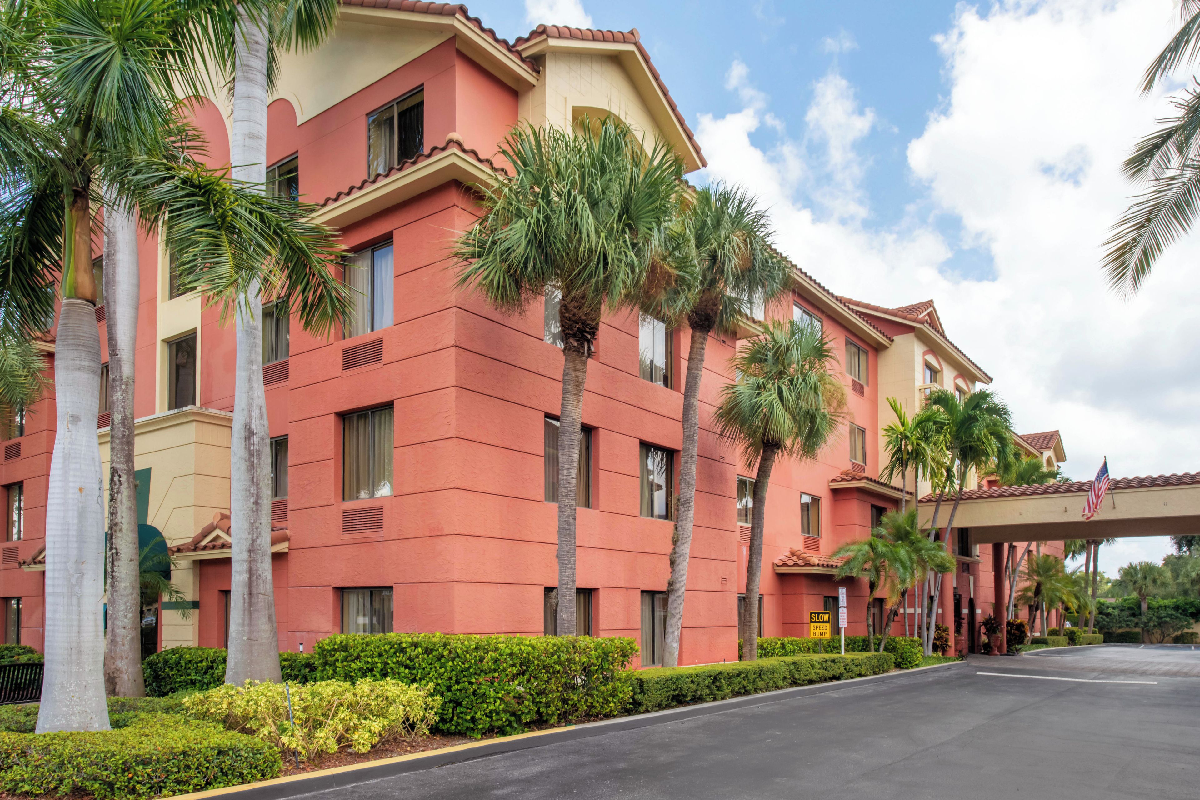 A multi-story hotel with a red facade, palm trees, and a clear sky.