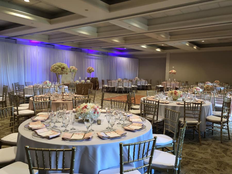 A banquet hall with round tables set for a formal event, featuring gold chairs and white tablecloths.
