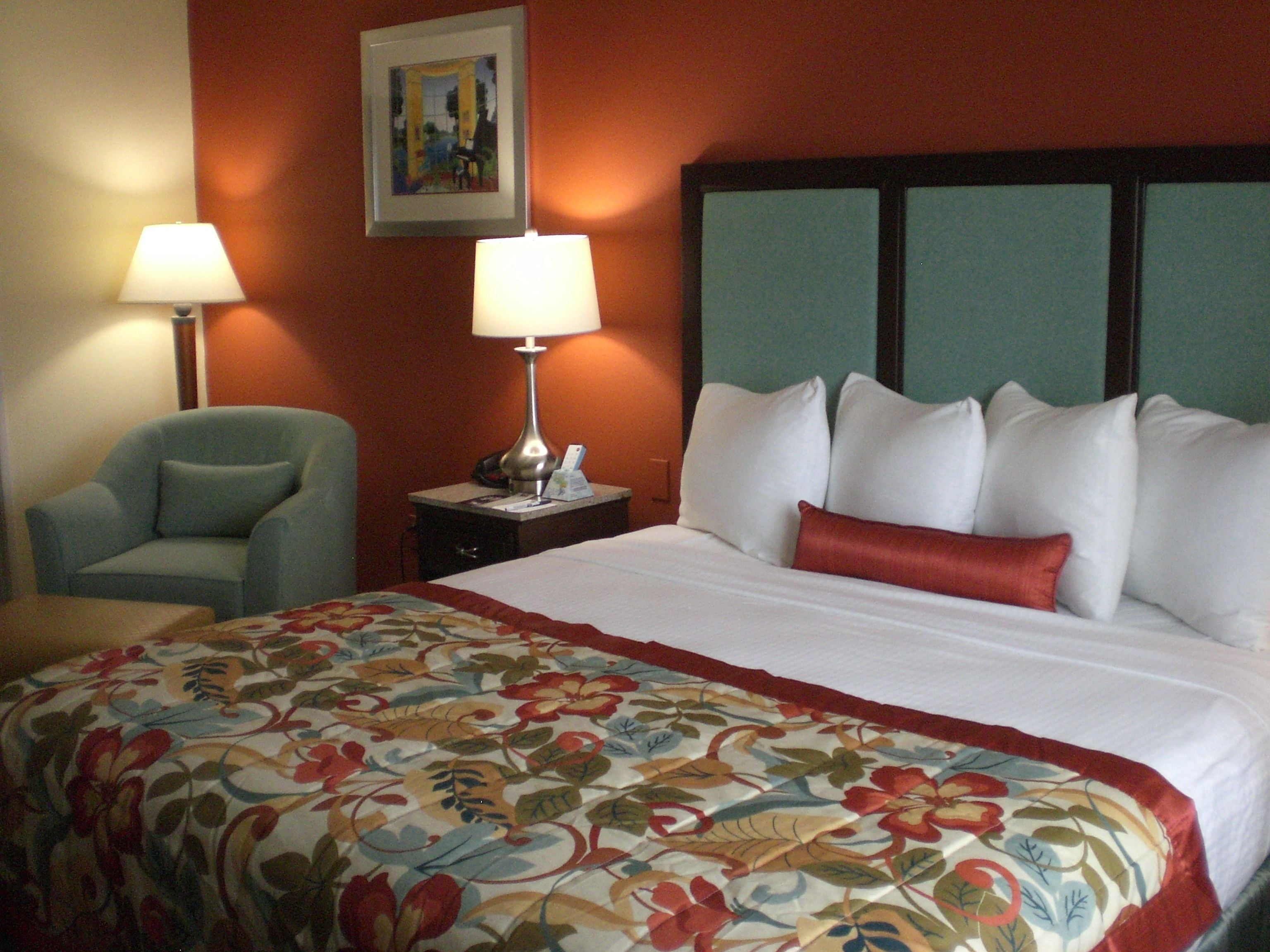A hotel room with a bed, a chair, a nightstand with a lamp, and a painting on the wall.