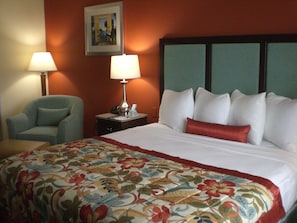 Une chambre d’hôtel avec un lit, une chaise, une table de chevet avec une lampe et un tableau au mur.