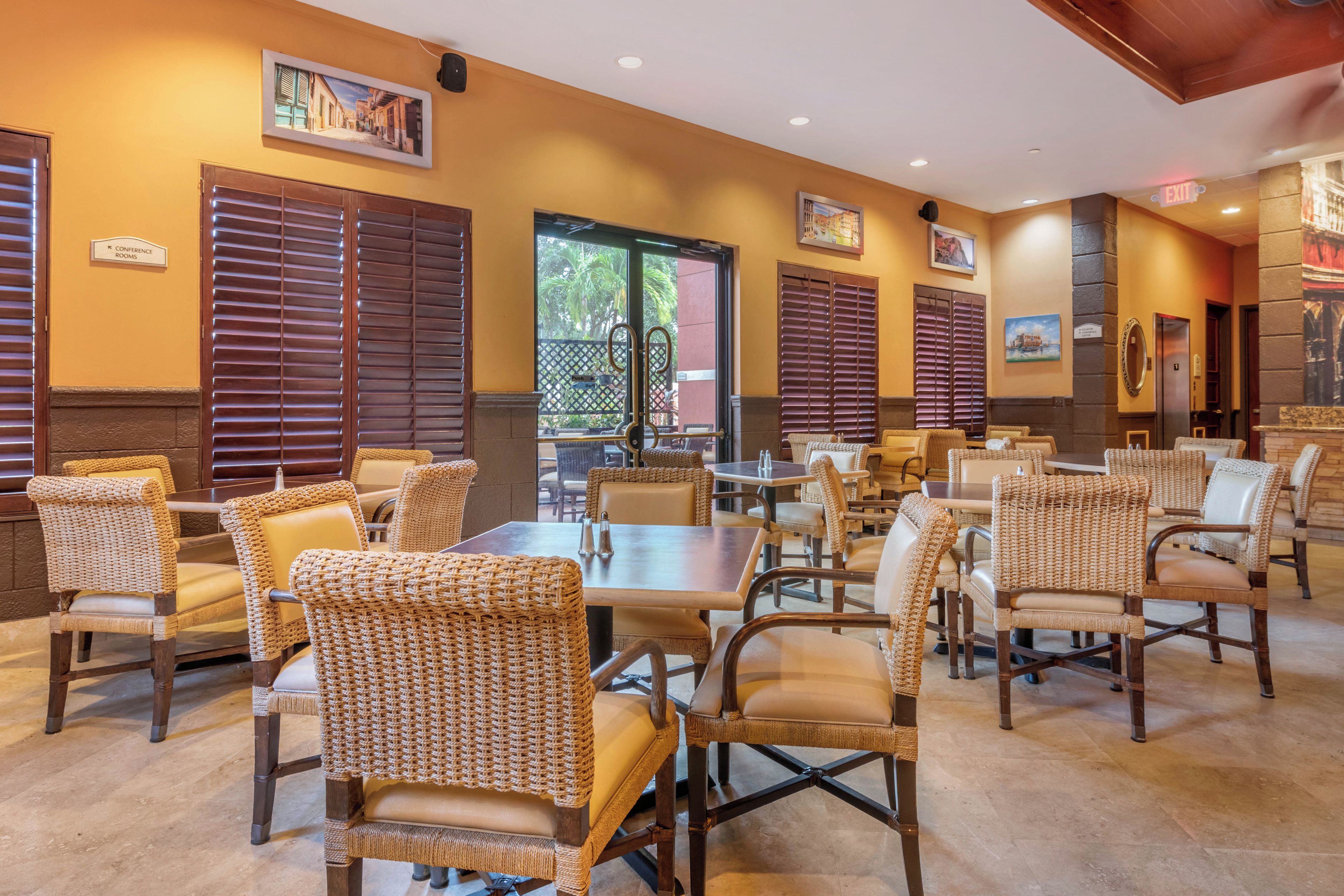 Un restaurant avec des chaises et des tables en osier, des stores en bois et des tableaux encadrés aux murs.