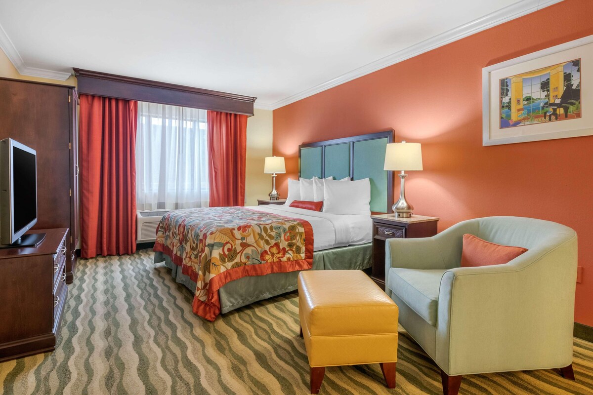 A hotel room with a bed, two bedside tables, a television, a chair, and a window with curtains.