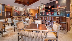 A restaurant with wicker chairs, wooden tables, a bar area, and a mural on the wall. - Best Western Plus Palm Beach Gardens Hotel & Ste & Conf Ctr (North Palm Beach)
