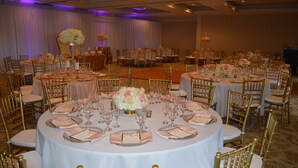 A banquet hall with round tables, gold chairs, and floral centerpieces. - Palm Beach Gardens & Suites Conference Ct (North Palm Beach)