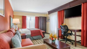 A hotel room with a bed, two sofas, a desk, a chair, a TV, and a window with curtains. - Best Western Plus Palm Beach Gardens Hotel & Ste & Conf Ctr (North Palm Beach)