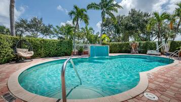 Una piscina con tobogán integrado, rodeada de palmeras y un seto.