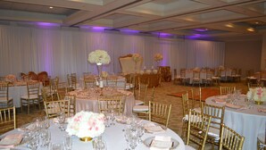A banquet hall with round tables, gold chairs, and white tablecloths. - Palm Beach Gardens & Suites Conference Ct (North Palm Beach)