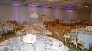 A banquet hall with round tables, gold chairs, and white tablecloths.