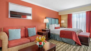 Une chambre d’hôtel avec un canapé, un lit, une table de chevet, une lampe et un vase de fleurs.
