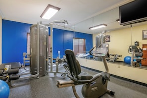 Een sportschool met diverse fitnessapparaten, waaronder een loopband, krachttoestellen en een spiegel die de ruimte weerspiegelt.