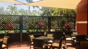 An outdoor patio area with wicker chairs and tables, a yellow canopy, and a lattice partition with plants. - Best Western Plus Palm Beach Gardens Hotel & Ste & Conf Ctr (North Palm Beach)