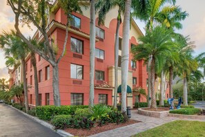 A multi-story hotel with a red facade, palm trees, and a landscaped garden. - Best Western Plus Palm Beach Gardens Hotel & Suites and Conference Ct (North Palm Beach)