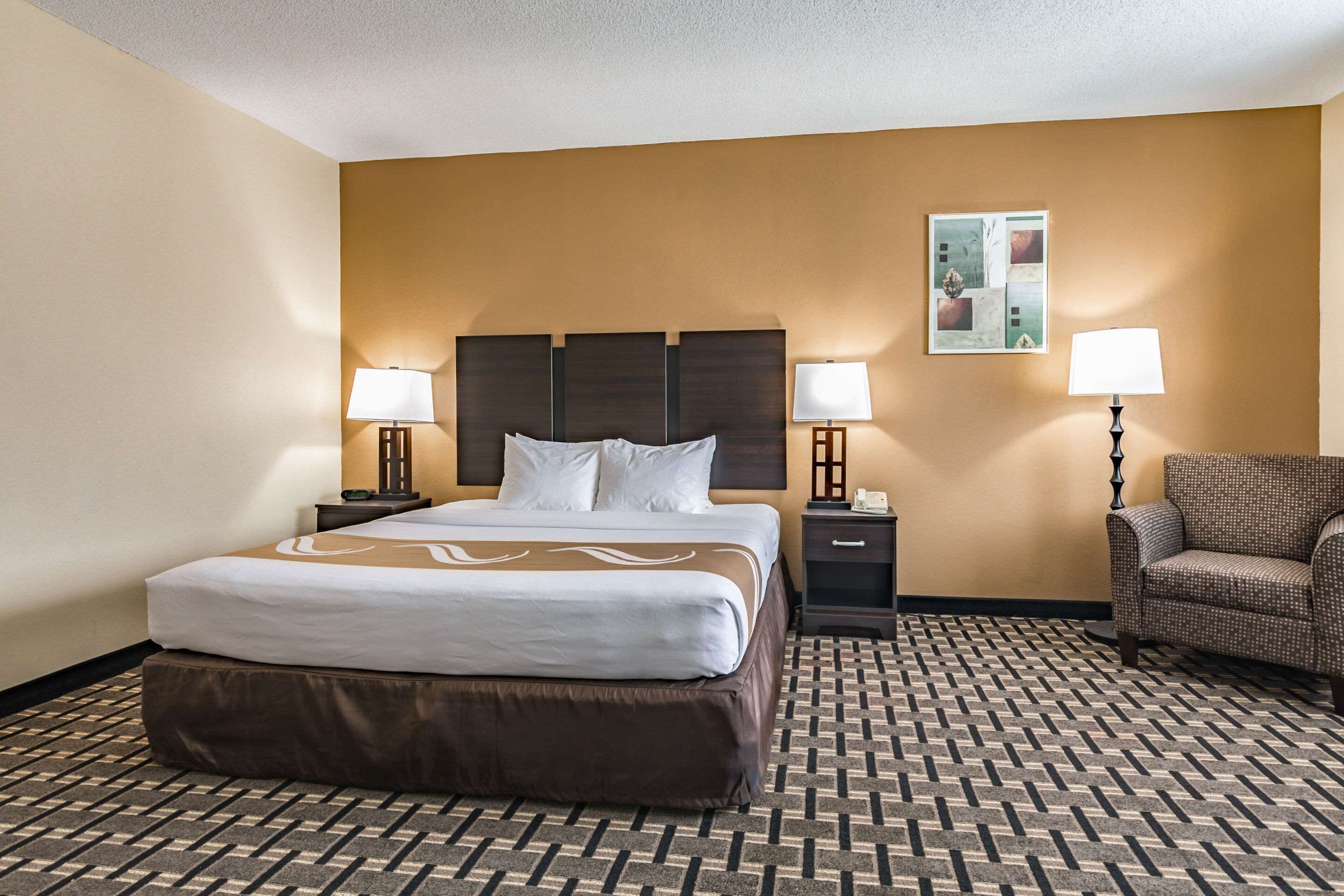 Une chambre d’hôtel avec un grand lit, deux tables de chevet avec des lampes, une chaise et une œuvre d’art accrochée au mur.